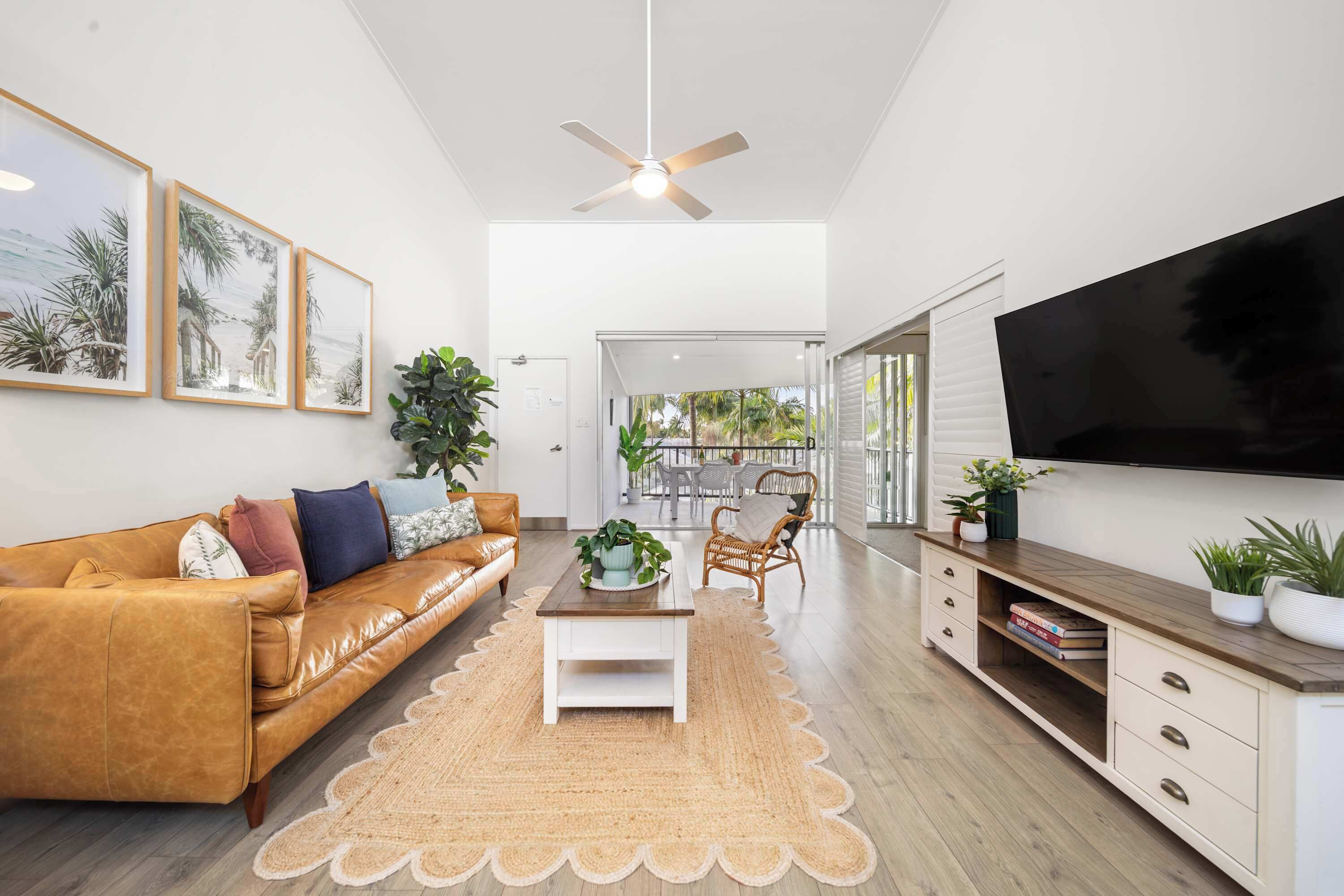 A modern living room with a leather sofa, a coffee table, a TV, and a ceiling fan.