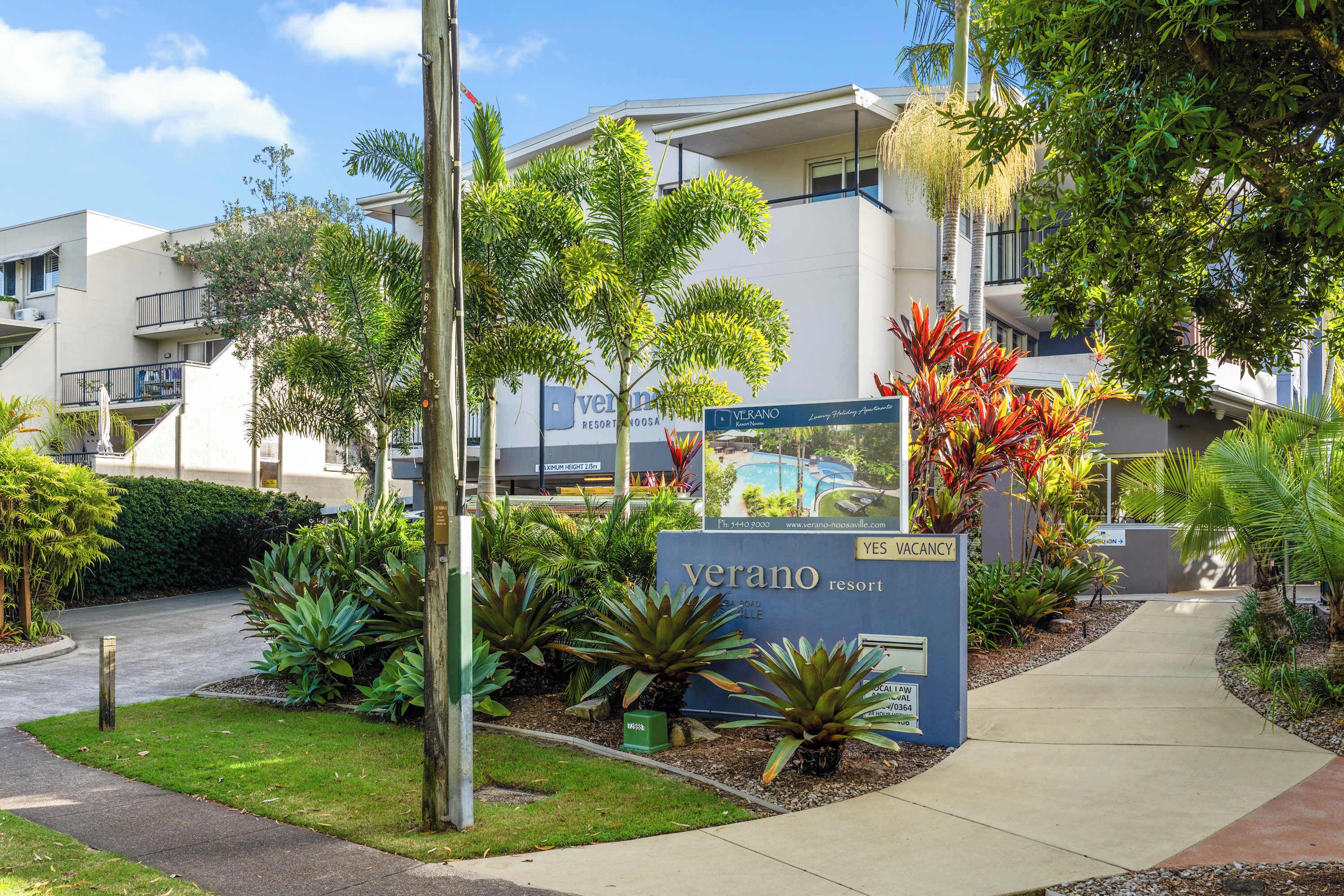 A sign for Verano Resort with a pathway and greenery.