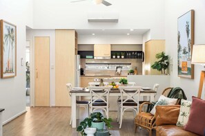 A modern kitchen with white cabinets, a dining area with white chairs, and a leather sofa with a cushion. - Elevated Noosa Escape: Heated Pool + Walk to River (Noosa Region)