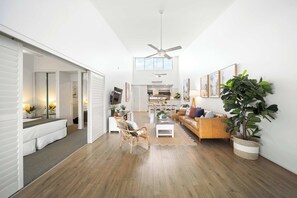 A spacious living area with a high ceiling, a ceiling fan, a wooden floor, a sofa, a coffee table, a chair, and a large plant. - Elevated Noosa Escape: Heated Pool + Walk to River (Noosa Region)