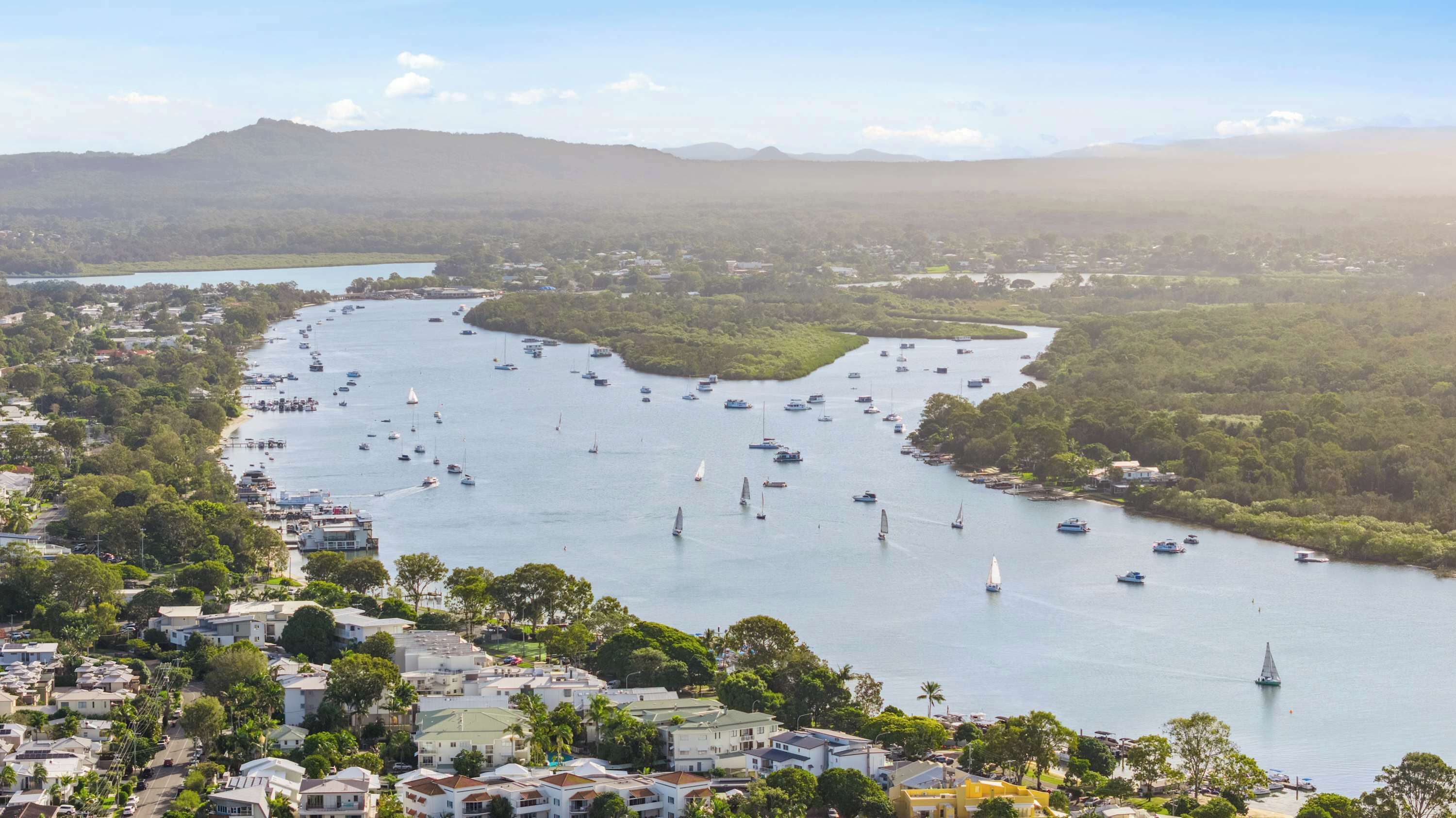 Un pueblo costero con un puerto deportivo lleno de barcos, rodeado de exuberante vegetación y edificios residenciales.
