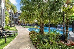 A pool area with lounge chairs, palm trees, and a building with balconies. - Elevated Noosa Escape: Heated Pool + Walk to River (Noosa Region)