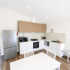 A modern kitchen with white cabinets, a stainless steel refrigerator, a microwave, a stove, and a sink.