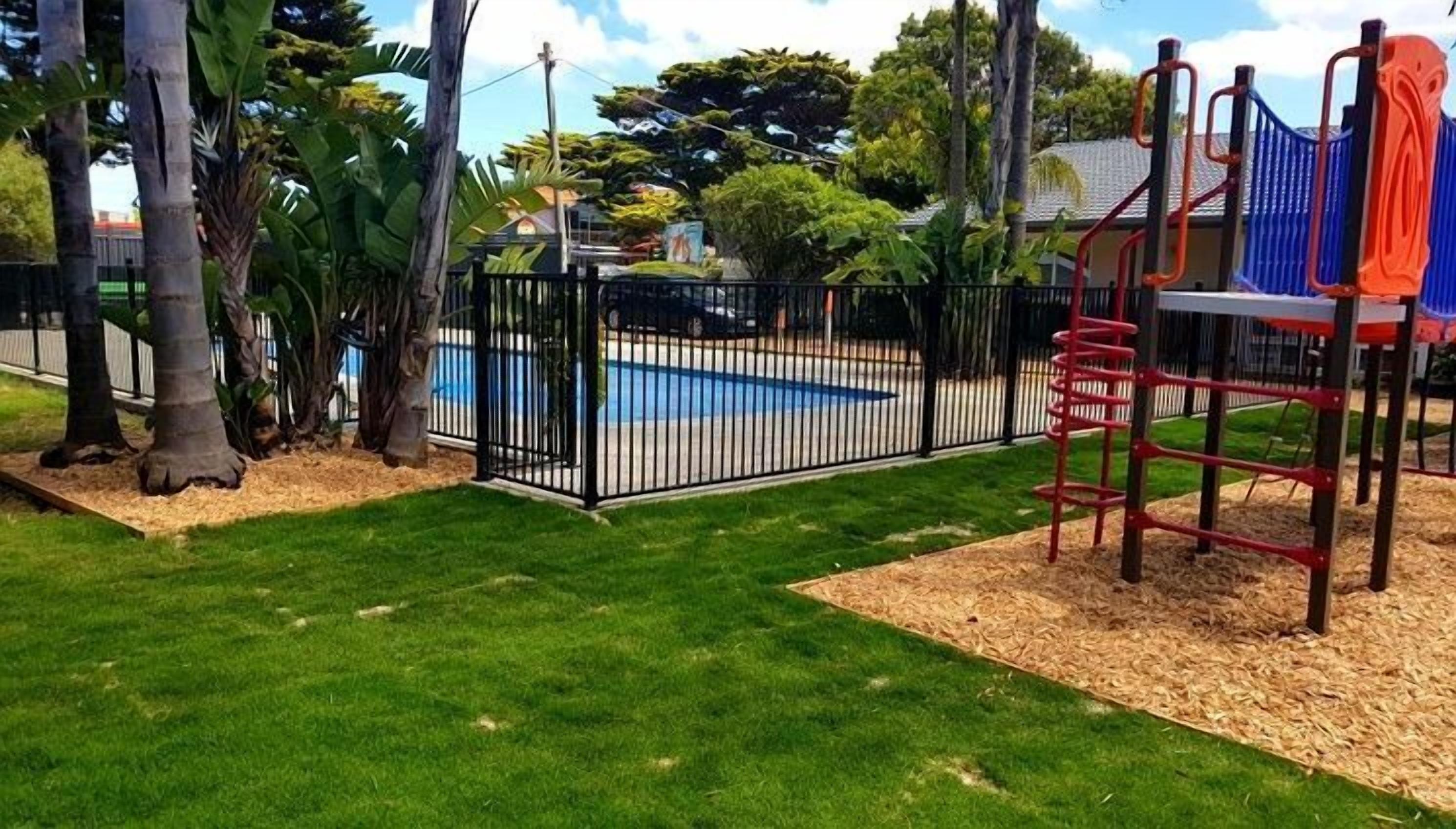 A fenced backyard with a pool, a playground, and a house in the background.