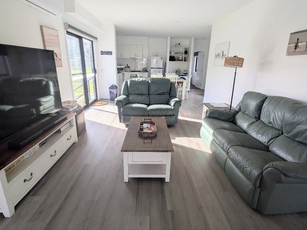 Una sala de estar con televisor, sofá, mesa de centro y un comedor al fondo.