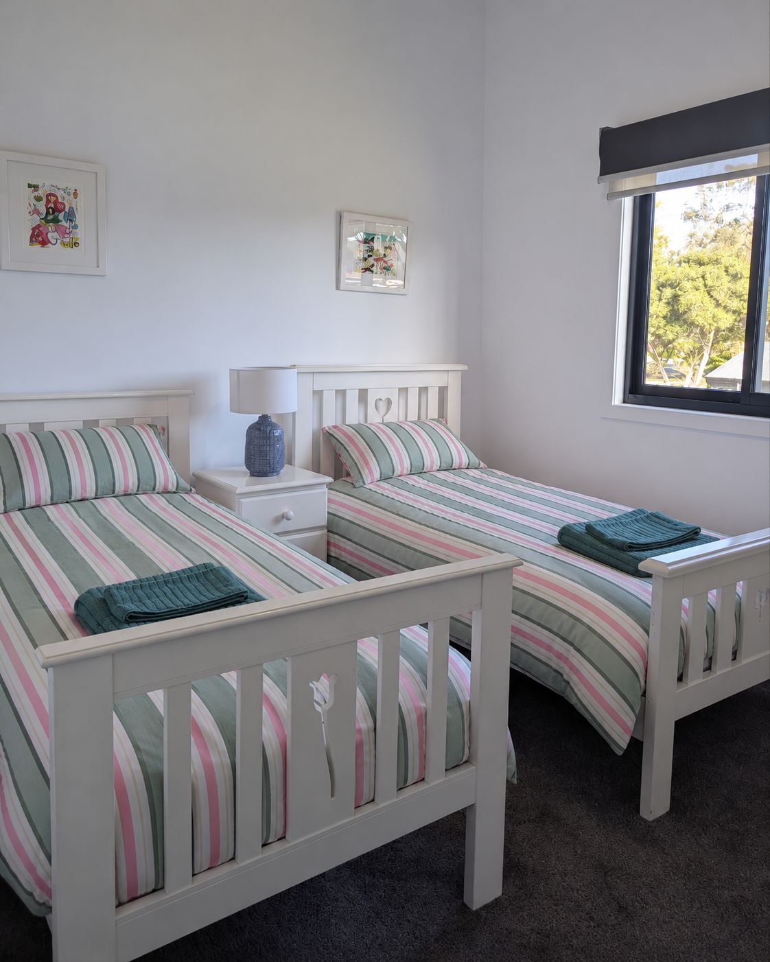 A bedroom with two single beds, a nightstand, a lamp, and a window with a view of trees.