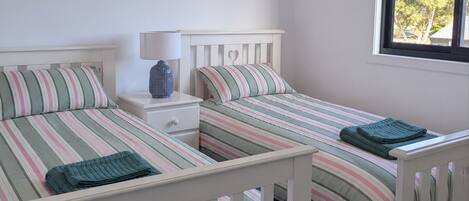 A bedroom with two single beds, a nightstand, a lamp, and a window with a view of trees.