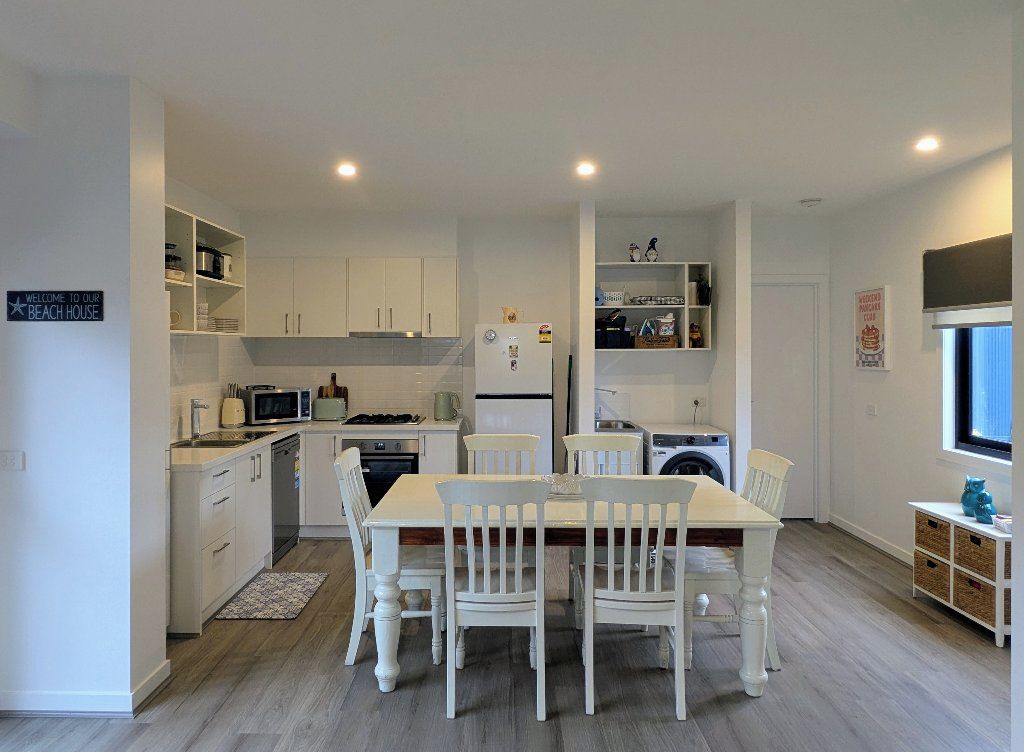 A modern kitchen with white cabinetry, a dining table with four chairs, and a built-in washing machine.