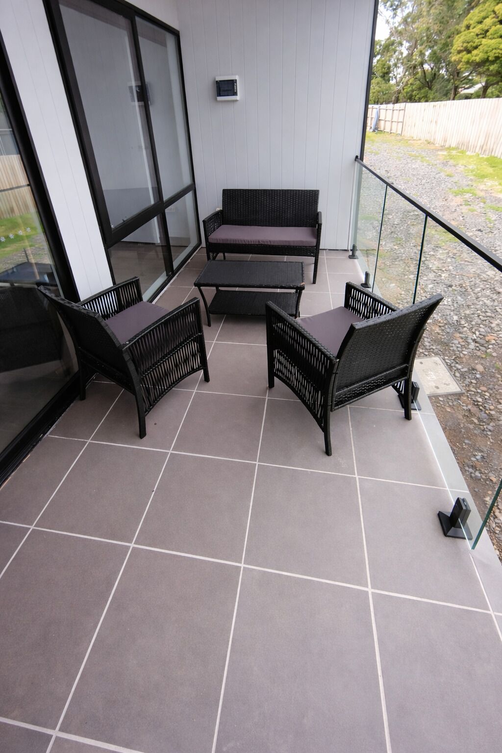 A balcony with a seating area consisting of two sofas and two chairs, a glass railing, and a tiled floor.