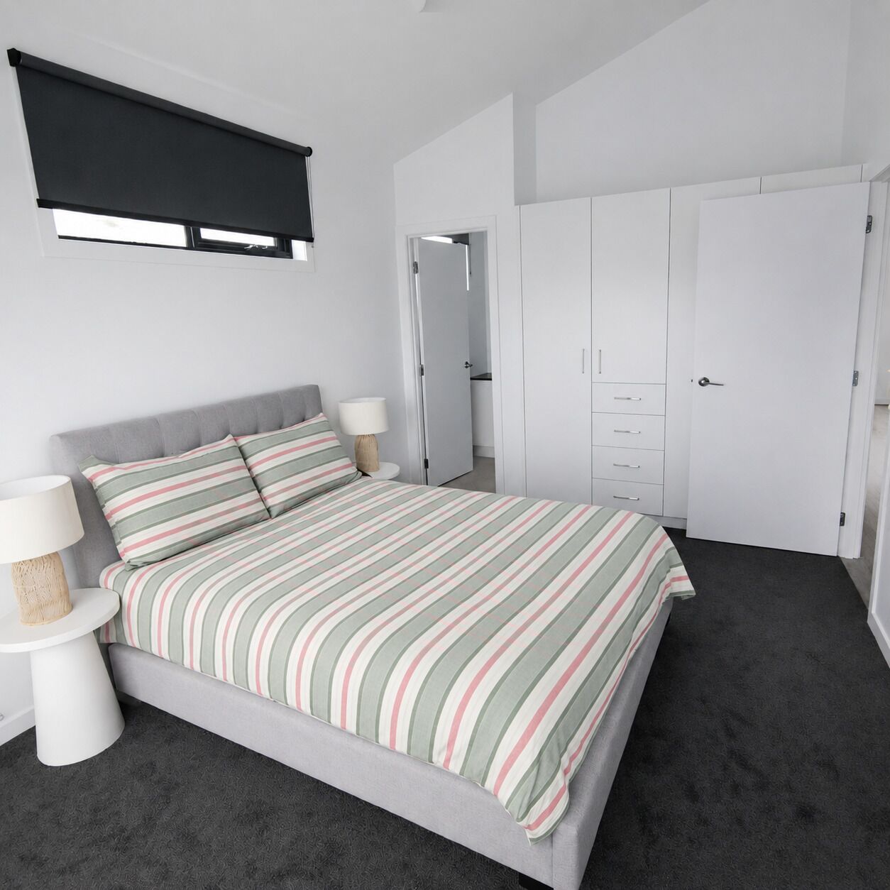 Un dormitorio con cama, mesitas de noche, un armario y una ventana con cortina.