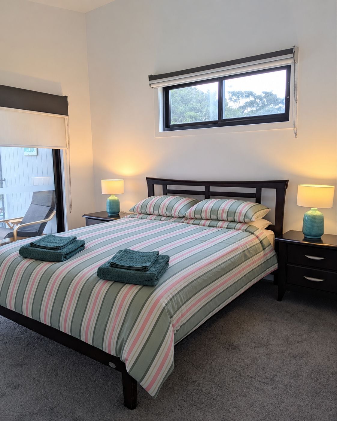 A bedroom with a bed, two bedside tables, a window, and a view of the outside.