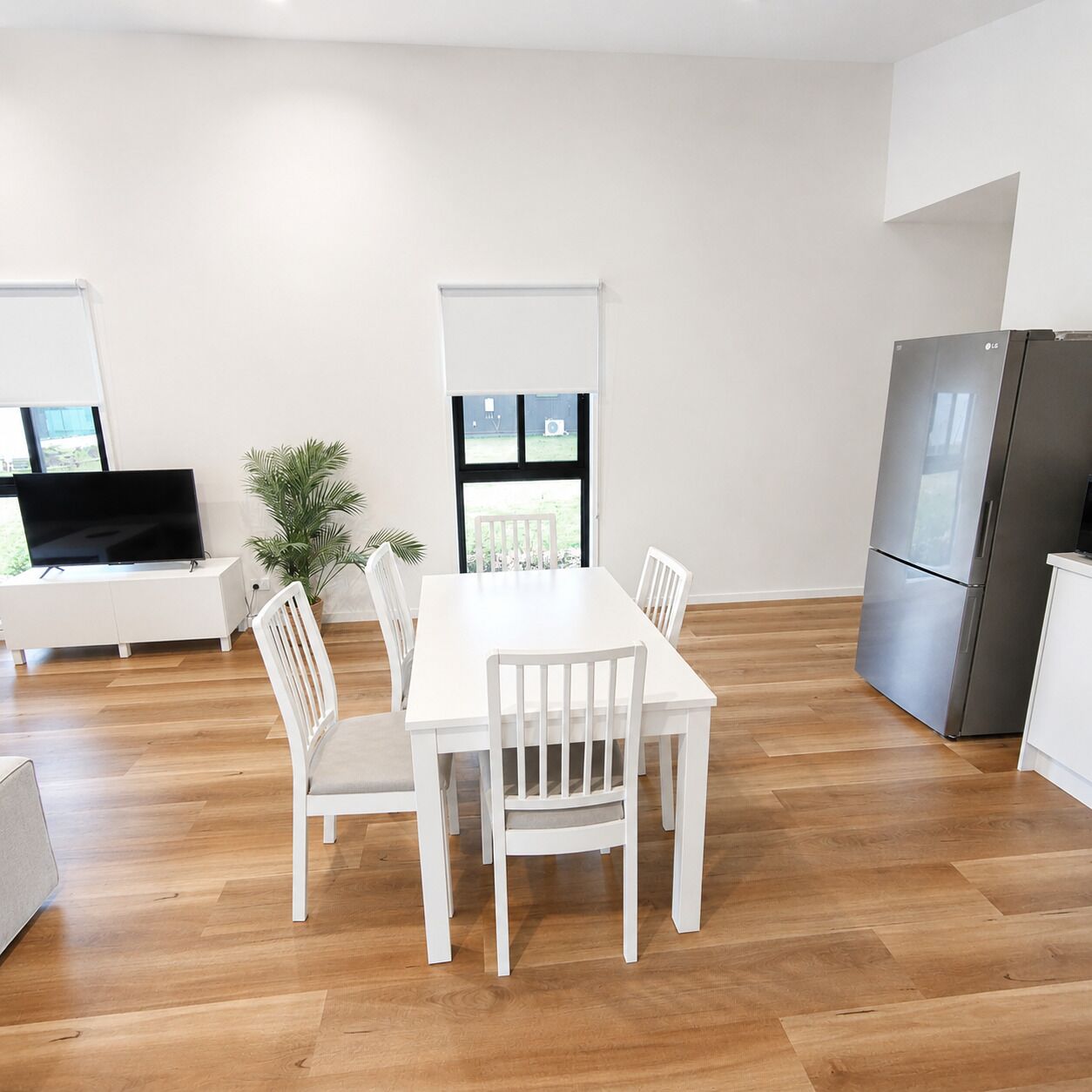 A modern kitchen with a white dining table, chairs, a TV, and a refrigerator.
