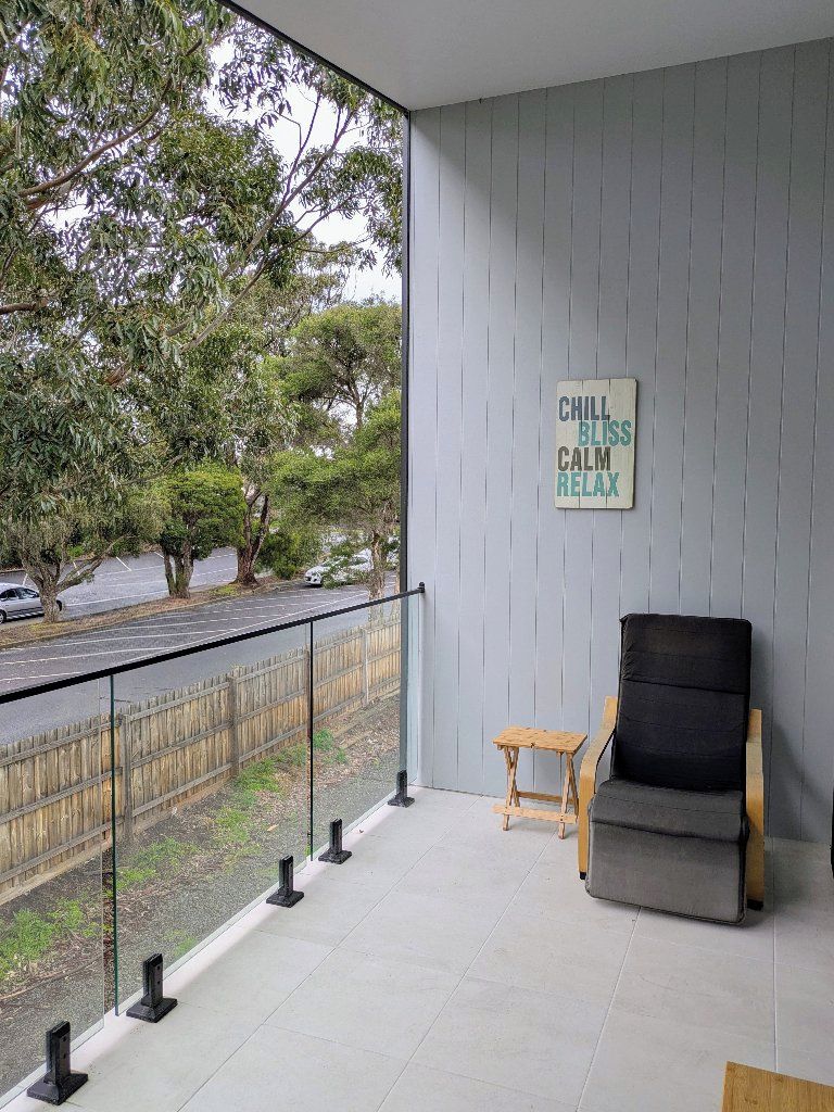 A balcony with a view of trees and a road, a chair, a small table, and a sign with the words 'CHILL BLISS CALM RELAX'.