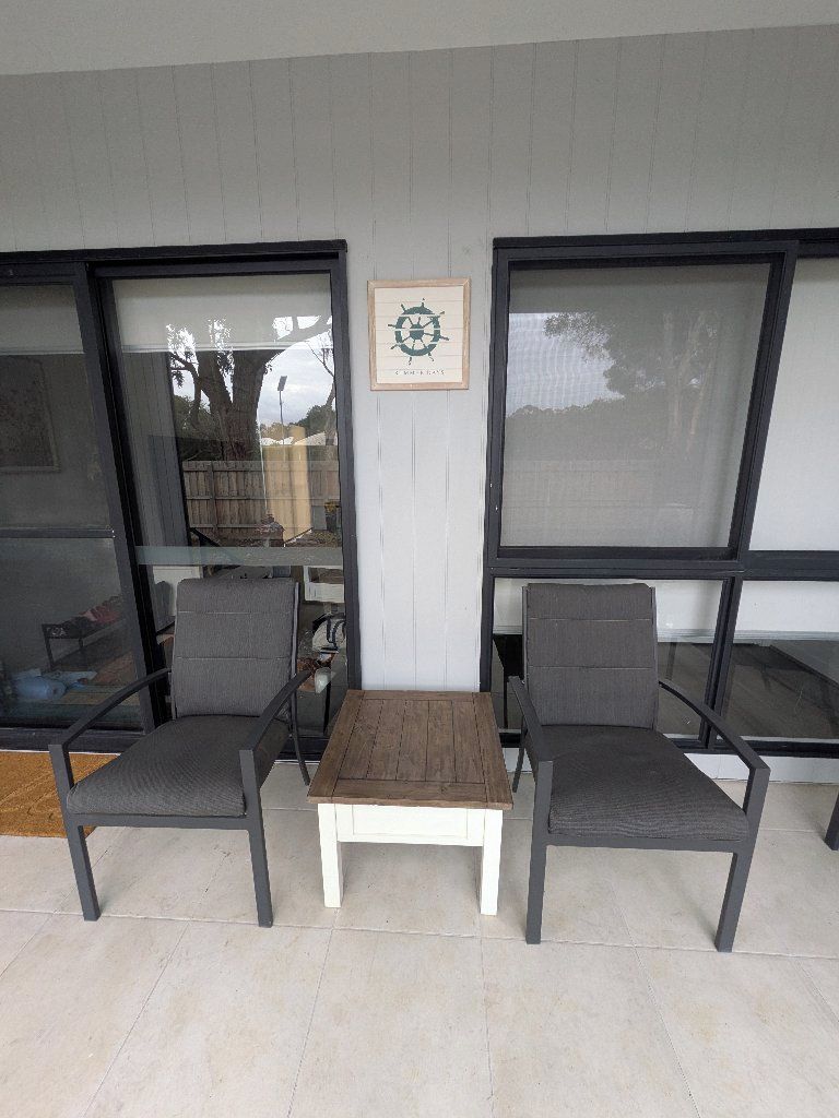 A patio area with two chairs and a small table, a framed picture on the wall, and large windows.