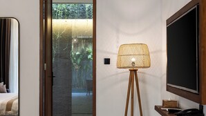 Une chambre moderne avec une porte vitrée donnant sur un jardin, un lampadaire et un téléviseur à écran plat posé sur une étagère en bois.