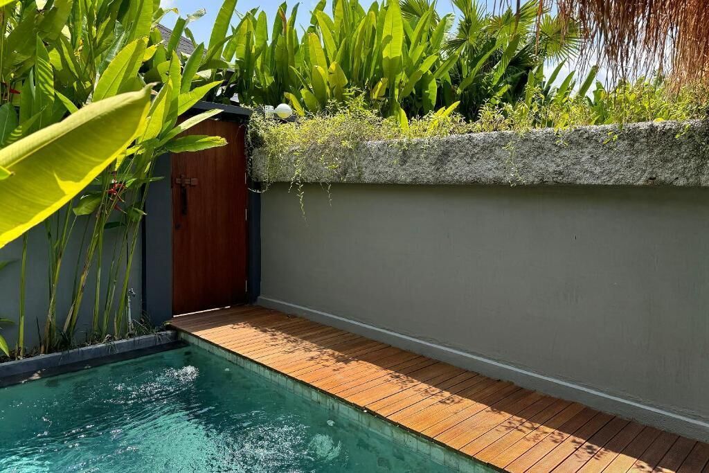 Une piscine dotée d’une terrasse en bois, entourée d’une végétation luxuriante et d’un mur de pierre.