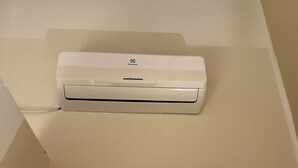 Un equipo de aire acondicionado blanco montado en una pared en una habitación con una viga de techo de madera.