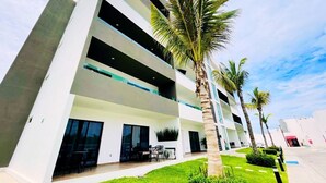 A modern multi-story building with balconies, a well-maintained lawn, and palm trees. - Marina Cerritos 507 Coastal Retreat – 2BR (Mazatlan)