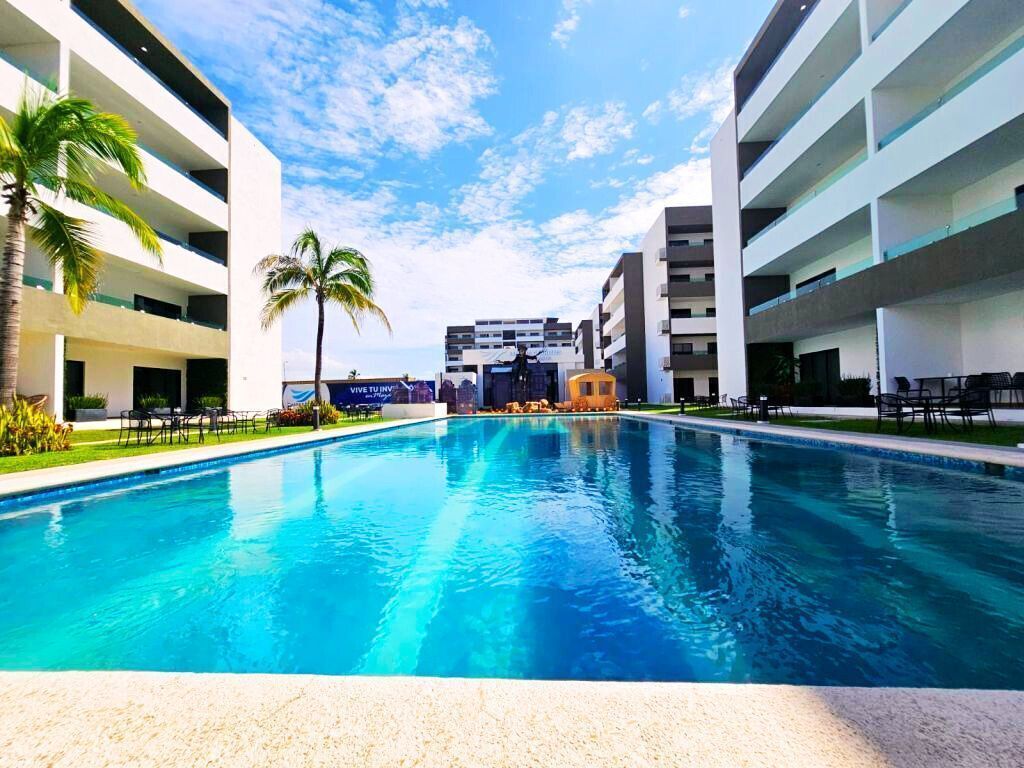 Une piscine à l’eau d’un bleu cristallin, entourée de bâtiments modernes et de palmiers.