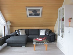 Ein modernes Wohnzimmer mit einem grauen Ecksofa, einem Glastisch und einer weißen Kommode mit Glastüren.