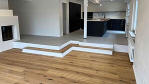 Un vaste espace de vie doté d’un plancher en bois, d’une cheminée intégrée et d’une cuisine équipée d’appareils électroménagers modernes.