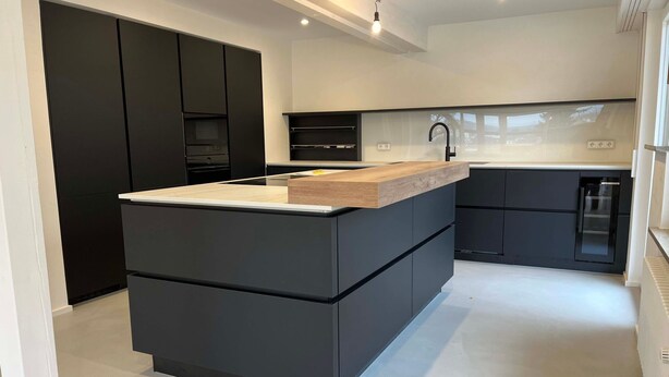 Une cuisine moderne dotée d’un îlot central, de meubles de couleur noire et d’un plan de travail blanc.
