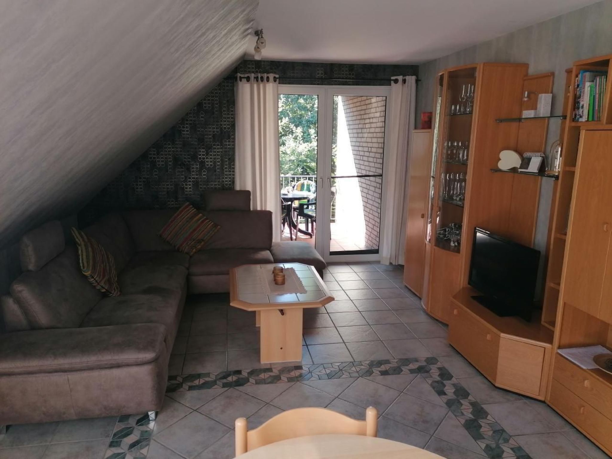 A living room with a sofa, a coffee table, a TV, and a bookshelf. There is a sliding glass door leading to an outdoor area.