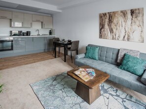 Ein modernes Wohnzimmer mit grauem Sofa, Couchtisch und Essbereich mit Tisch und Stühlen.