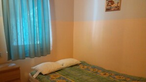 Ein kleines Schlafzimmer mit einem Einzelbett, einem Nachttisch und einem Fenster mit blauen Vorhängen.