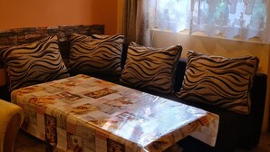 Ein gemütlicher Wohnbereich mit einer Couch, verziert mit Kissen im ZEBRA-MUSTER, einem Tisch mit einem gemusterten Tischläufer und einem Fenster mit Spitzenvorhängen.