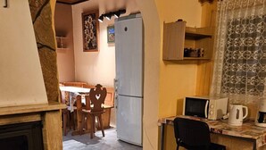 Ett mysigt kök med en stenöppen spis, en matplats med trästolar och en köksbänk med mikrovågsugn och kaffebryggare.