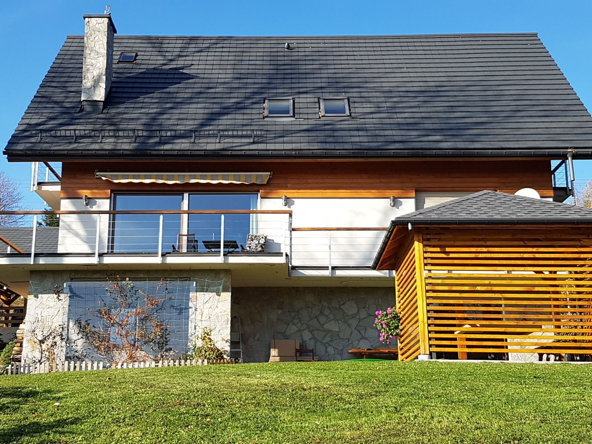 Une maison à deux étages avec des fondations en pierre, un balcon doté d’une balustrade et une terrasse en bois.