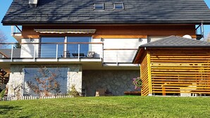 Une maison à deux étages avec des fondations en pierre, un balcon doté d’une balustrade et une terrasse en bois.
