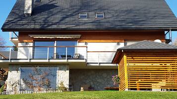 Une maison à deux étages avec des fondations en pierre, un balcon doté d’une balustrade et une terrasse en bois.