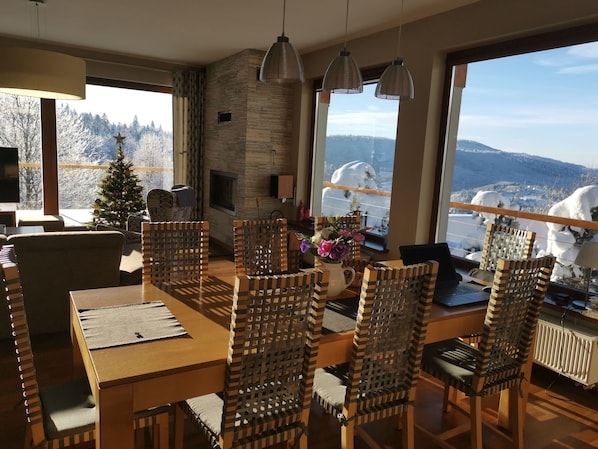 A dining area with a wooden table and chairs, a fireplace, and a view of snowy mountains.