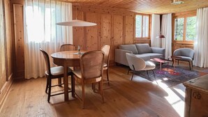 A wooden cabin interior with a dining table, chairs, a sofa, and a small coffee table. - Curtin Duas by Interhome (Fex / Fextal (Sils im Engadin)