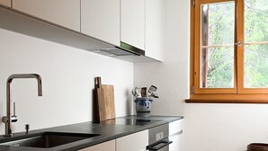 A modern kitchen with white cabinets, a black countertop, and a window with a view of greenery. - Curtin Duas by Interhome (Fex / Fextal (Sils im Engadin)