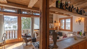 A cozy cabin interior with a wooden interior, a fireplace, a dining area, and a bar with bottles. - Chesa Cavril by Interhome (Maloja)