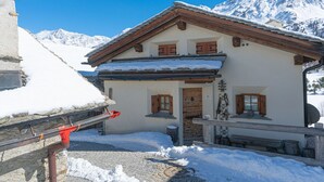 A two-story chalet with a wooden facade, a snow-covered roof, and a mountain backdrop. - Chesa Cavril by Interhome (Maloja)