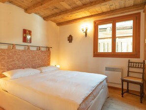 A bedroom with a wooden ceiling, a bed with white linens, a window with wooden shutters, and a wall-mounted light fixture. - Chesa Cavril by Interhome (Maloja)