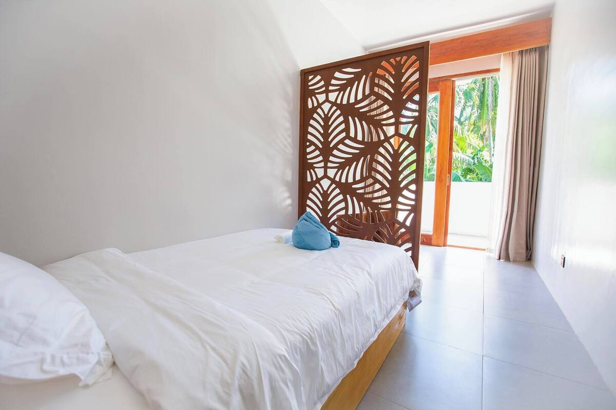 Un dormitorio con una cama, una almohada azul, un panel decorativo de madera y vistas a zonas verdes.