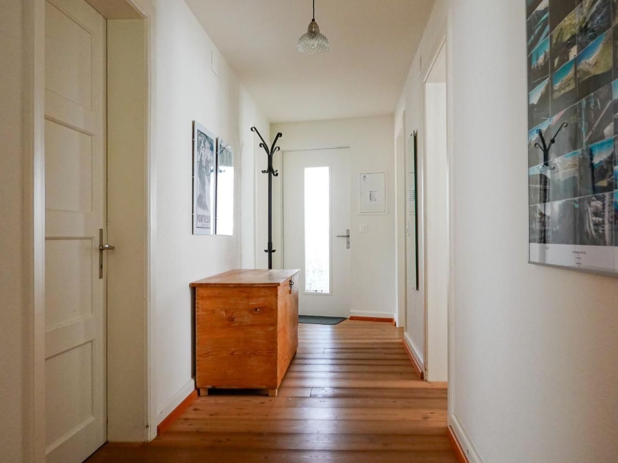Un couloir avec un plancher en bois, une commode en bois et une porte au fond.