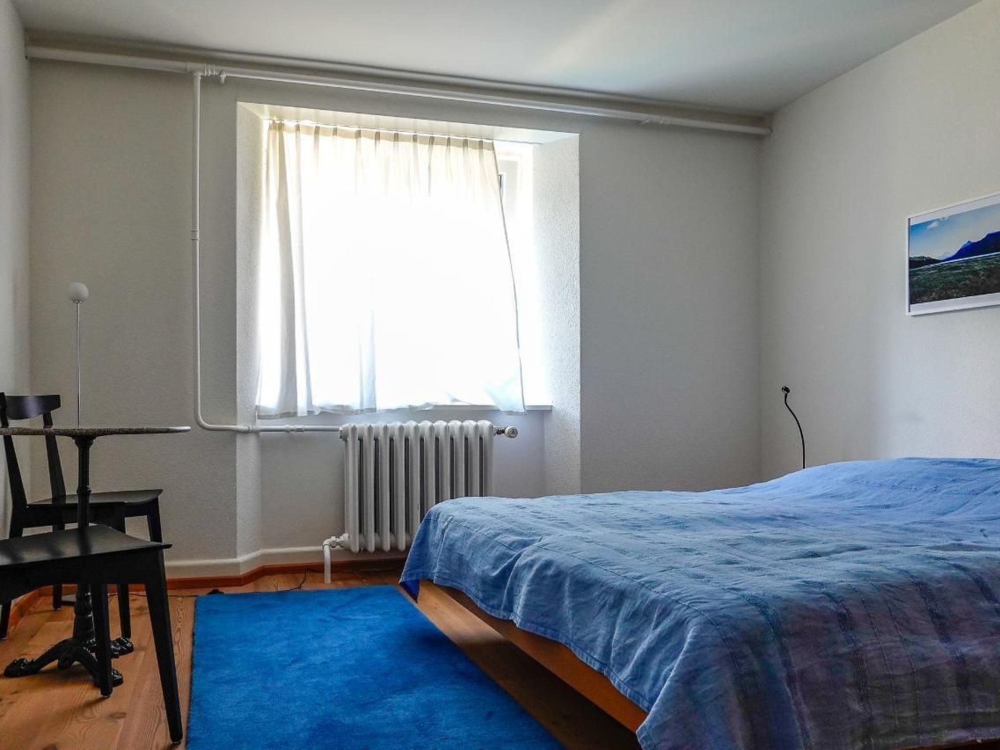 Ein Schlafzimmer mit Bett, Stuhl, Heizkörper und einem Fenster mit Vorhängen.