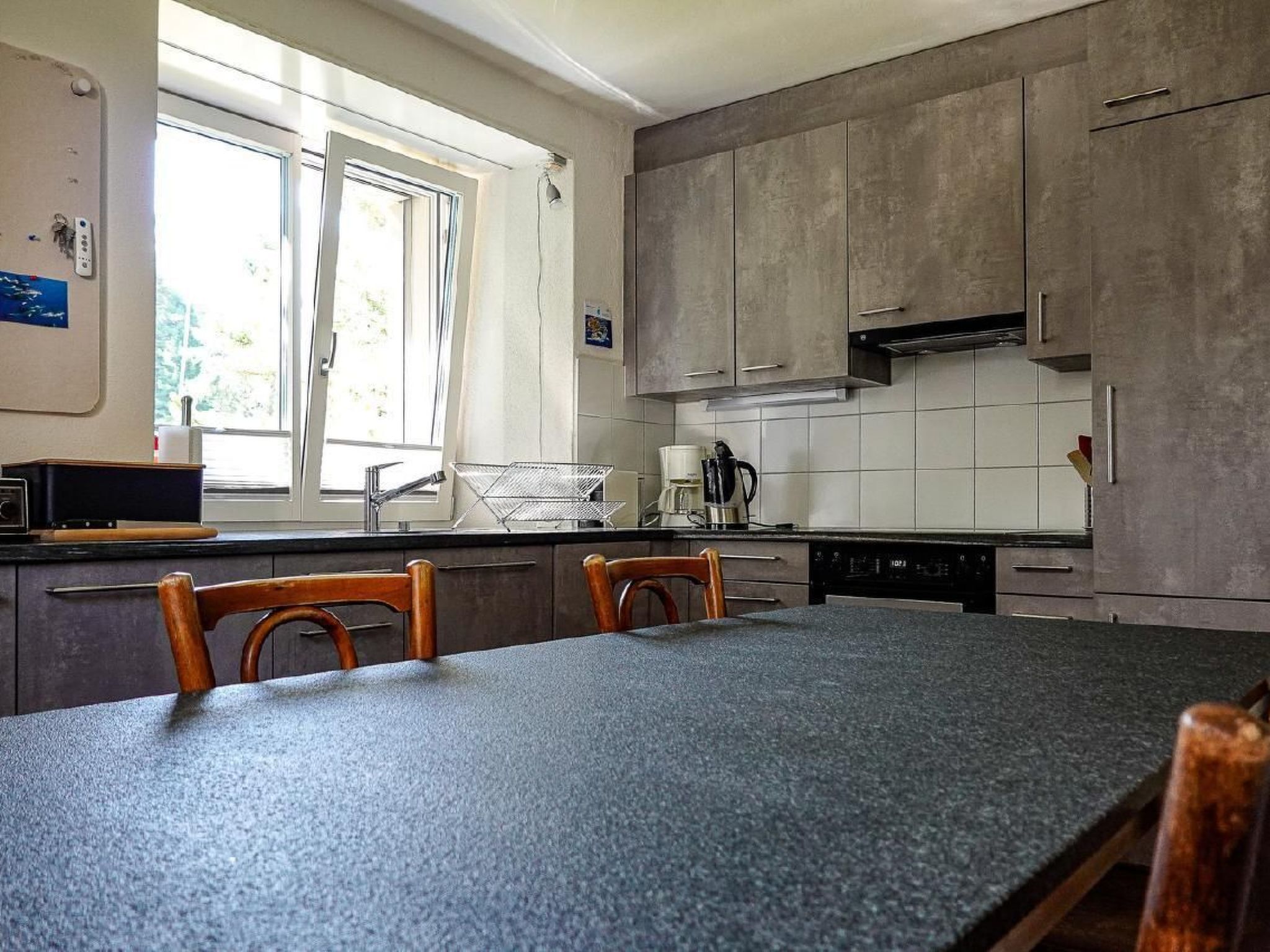 Een keuken met een granieten aanrecht, houten stoelen, een koffiezetapparaat en een vaatwasser.