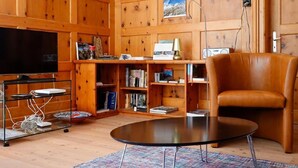 Ein gemütliches Wohnzimmer mit Ledersessel, Flachbildfernseher, Bücherregal und einem kleinen Tisch.