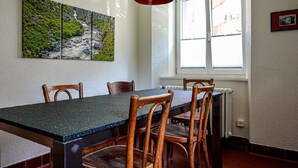 Ein Essbereich mit Tisch und Stühlen, einem Fenster mit Jalousien und einem Gemälde an der Wand.