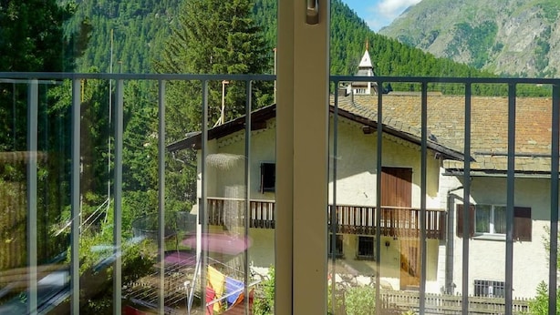 Blick auf Berge vom Balkon, mit einem Haus im Hintergrund.