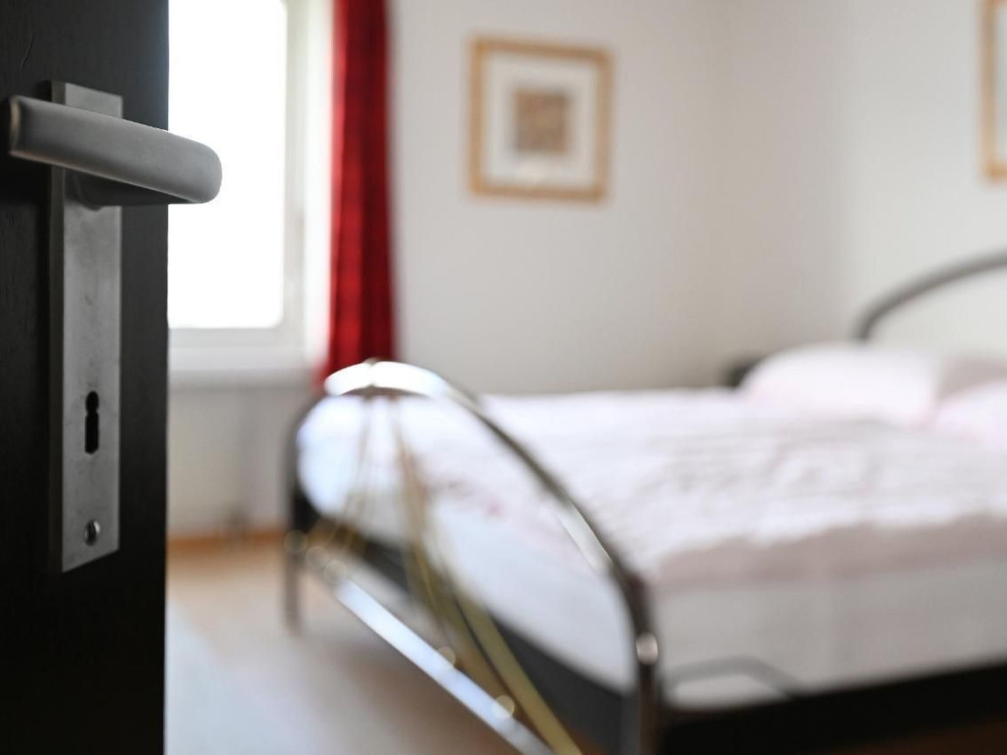 Une chambre à coucher avec un lit, une fenêtre ornée de rideaux rouges et un tableau encadré accroché au mur.