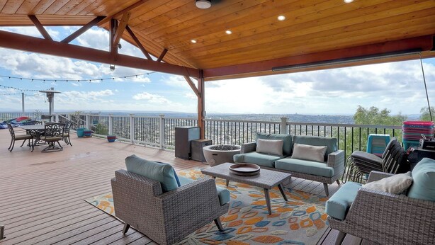 Eine überdachte Terrasse mit Korbmöbeln, einem Esstisch und Blick auf die Stadtlandschaft.