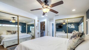 Ein Schlafzimmer mit einem großen Bett, zwei Nachttischen, einem Deckenventilator, einem Spiegel und einer Steinwand.